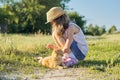 Girl child in hat on country road plays with red cat, sunny summer day rustic style Royalty Free Stock Photo