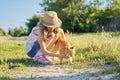 Girl child in hat on country road plays with red cat, sunny summer day rustic style Royalty Free Stock Photo