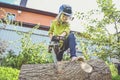 The girl child in a helmet with an electric saw saws a log