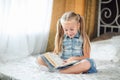 Girl child in denim sundress lay bed read book. Kid prepare to go to bed. Pleasant time in cozy bedroom. Girl kid long hair, relax