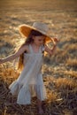 Girl child with long hair walking across the field wearing a hat