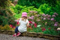 Girl child relaxing in  flower garden rear view. Adorable little kid sitting around growing flowery. Young caucasian female child Royalty Free Stock Photo