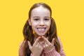 Girl child shows the first molar and smiles on a yellow background