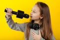 Girl child sings a song in karaoke. Holds a microphone in his hand, a portrait on a yellow background