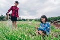 Girl child sitting in organic vegetables garden and blurred boy watering the plants on sky background in rural or countryside Royalty Free Stock Photo