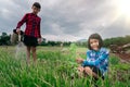 Girl child sitting in organic vegetables garden and blurred boy watering the plants on sky background in rural or countryside Royalty Free Stock Photo