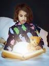 Girl, child and surprised for book with magic in bed for fantasy story, sparkle and imagination with teddy bear. Kid Royalty Free Stock Photo