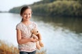 The girl child with toy bear walking along the path in the forest at sunset, beautiful river and landscape Royalty Free Stock Photo