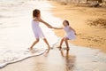 Girl in white dresses playing on beach. older sister pulls younger into water