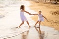 Girl in white dresses playing on beach. older sister pulls younger into water