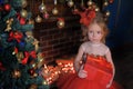 Girl at the Christmas tree in a red elegant dress with a box with gifts in her hands Royalty Free Stock Photo