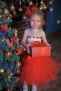 girl at the Christmas tree in a red elegant dress with a box with gifts in her hands Royalty Free Stock Photo