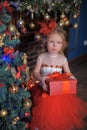 Girl at the Christmas tree in a red elegant dress with a box with gifts in her hands Royalty Free Stock Photo