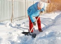 Girl cleans snow shovel on the site near his house. sunlight