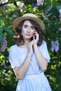 A girl with clear skin and wavy brown hair in a straw hat in a lilac garden in bloom. Beautiful calm girl portrait. Allergy, sprin Royalty Free Stock Photo