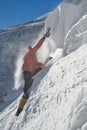 Girl climber climbs a snow cornice using ice axes through snow blown away by the strong wind. Royalty Free Stock Photo