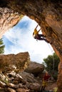 The girl climbs the rock in the shape of an arch, A man is belaying a climbing partner