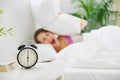 Girl closing ears by pillow to avoid hearing clock Royalty Free Stock Photo