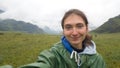 A girl in cloudy rainy weather takes a selfie while riding a horse on a picturesque field. Foggy weather. Green hills