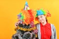 A girl in a clown wig stands next to a funny New Year`s Christmas tree Royalty Free Stock Photo