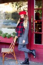 Girl in coat and a red beret with long curls stands thoughtfully near a cafe on a background of a red facade Royalty Free Stock Photo