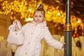 Girl in coat stands, leaning one hand on lamp post