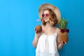 Girl with coconut cocktail and pineapple in a sun hat and glasses on a blue background, woman with a tropical cocktail on vacation Royalty Free Stock Photo