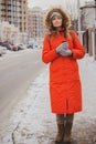 Girl with coffee in warm jacket with fur hood on the street. Winter fashion. Pretty woman in orange hooded jacket in the city. Royalty Free Stock Photo