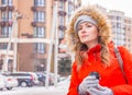 Girl with coffee in warm jacket with fur hood on the street. Winter fashion. Pretty woman in orange hooded jacket in the city. Royalty Free Stock Photo
