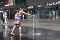 A girl in a colorful bright dress plays with splashes of water fountain in the city square. Mogilev, Belarus - June, 21 2021