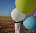 Girl in a field hiding face behind balloons Royalty Free Stock Photo