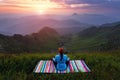 The girl on colorful mat is practicing Yoga. Beautiful mesmerising sunrise, orange sky with clouds, high mountains in fog. Summer. Royalty Free Stock Photo