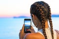A girl contemplates the sunset taking a shot with her smartphone