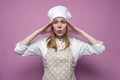 Girl cook in apron hold hands behind head on pink background, woman housewife in kitchen clothes in stress Royalty Free Stock Photo