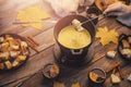 Girl cooks gourmet Swiss fondue dinner with cheese on fire, autumn wooden background with maple leaves. Top view, flat