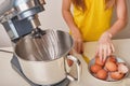 A girl cooks homemade cake in the kitchen, beats eggs in a mixer on the kitchen table. Hands break eggs. Against the