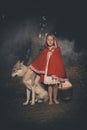 Girl in costume of little red riding hood in forest posing with wolf dog Royalty Free Stock Photo