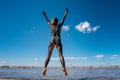 A girl covered with medical mud jumps against the background of the sea