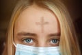 Girl with cross made from ash on forehead with face mask. Ash wednesday concept. Royalty Free Stock Photo