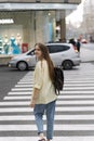 Girl crosses the road at the pedestrian crossing looking over her shoulder. Teenager against the backdrop of busy street Royalty Free Stock Photo