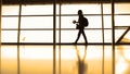 The girl with cup of coffee going in airport in front window opposite the runway, silhouette, warm