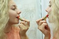 A girl with curly hair paints her lips with red lipstick in front of the mirror at home. Close up. Selective focus Royalty Free Stock Photo