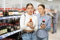 Girl customer with female friend is thinking about buying spicy and unusual soy sauce.