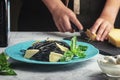 Girl cuts cheese to decorate black spaghetti dishes. Unusual cuttlefish ink pasta. A wholesome light dinner with basil