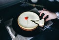 Girl cuts with knife classical vanilla New York cheesecake on dark-violet plate on wooden tray with rope handles. Small red heart Royalty Free Stock Photo