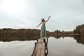A girl is dancing on a wooden bridge against the backdrop of a forest lake. Royalty Free Stock Photo