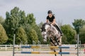 Girl on a dapple gray horse practicing jumping over a fence