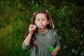 A girl with dark hair on a background of green foliage launches soap bubbles. Summer outdoor activities. Blow a soap bubble