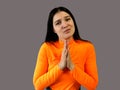 Girl with dark hair in a bright orange sweater on a gray background. implore