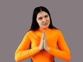 Girl with dark hair in a bright orange sweater on a gray background. implore